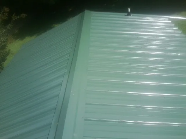 New green metal panels meeting at the ridge of a roof — Flat Roof Repair work by our crew in Masontown