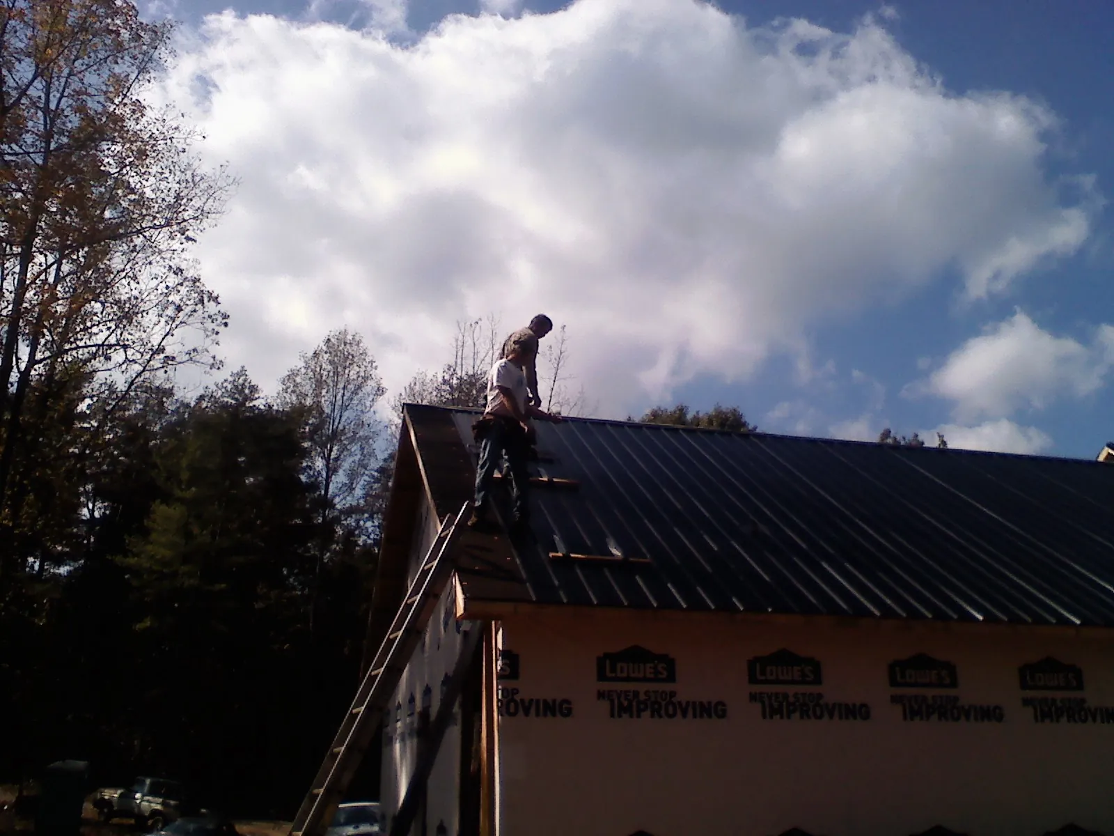 Roofer fastening dark metal panels high against a cloudy sky, from a Roof Inspection job in Masontown