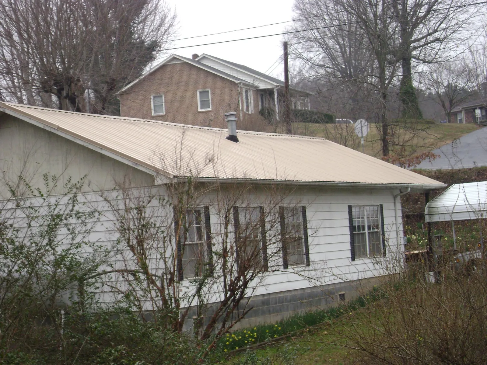 Tan metal roof on a white sided house set into a hillside — Commercial Roofing by Roofing Brothers in Masontown